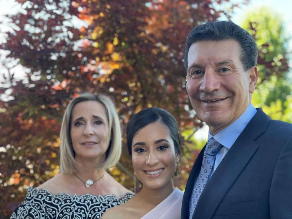 A 2024 outdoor family portrait of Lisa, Olivia, and Roy Spagnolo standing together, smiling in formal attire against a backdrop of colourful trees, celebrating the strength and legacy of the Spagnolo family.