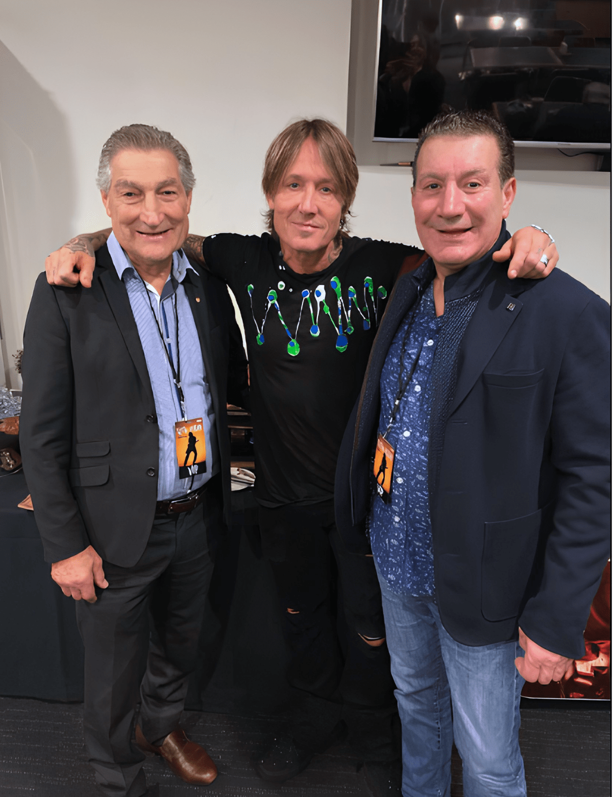 Roy Spagnolo and Bill Calabria pose with internationally renowned musician Keith Urban backstage at a concert, smiling together while wearing event passes.
